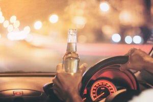 Drunk young man drives a car with a bottle of beer. Raleigh, NC