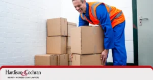 Greensboro worker holding their lower back after picking up a box on the job